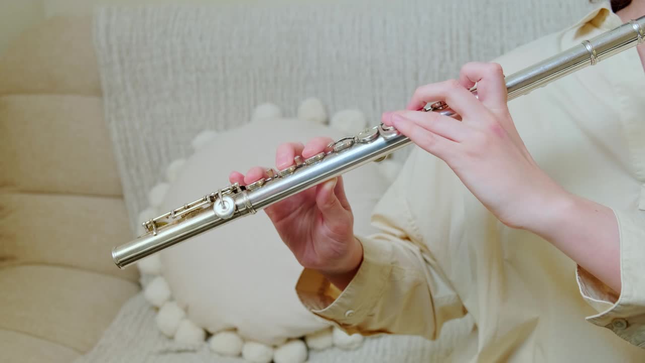 一个女人手拿长笛在家里客厅的沙发上演奏，特写镜头视频下载