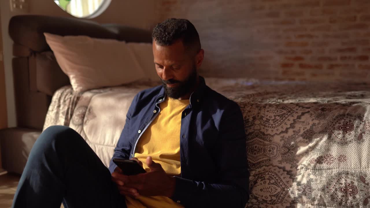 一个成熟的男人坐在家里的地板上用智能手机视频下载
