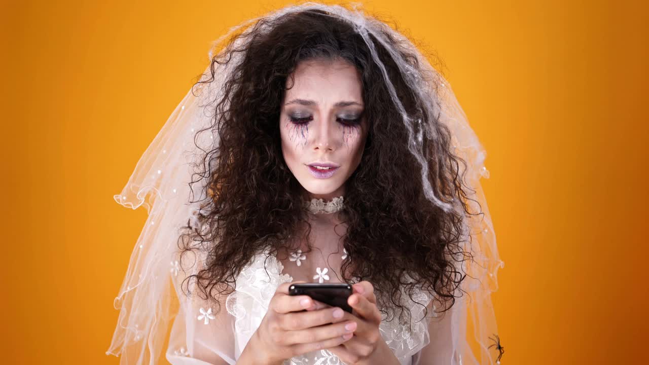 在万圣节，哭丧的新娘穿着婚纱，化着妆，用智能手机视频素材