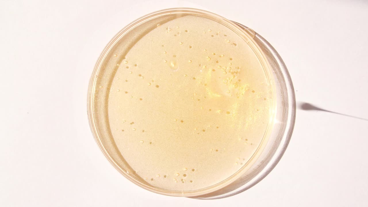 黄色透明化妆品凝胶霜与分子泡沫流动在平原的白色表面。微距镜头视频下载
