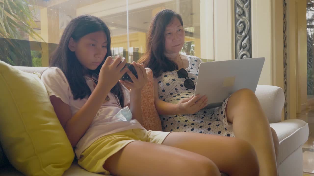 亚洲母亲使用笔记本电脑在酒店大堂工作期间与女儿度假，工作任何地方的生活理念。视频素材