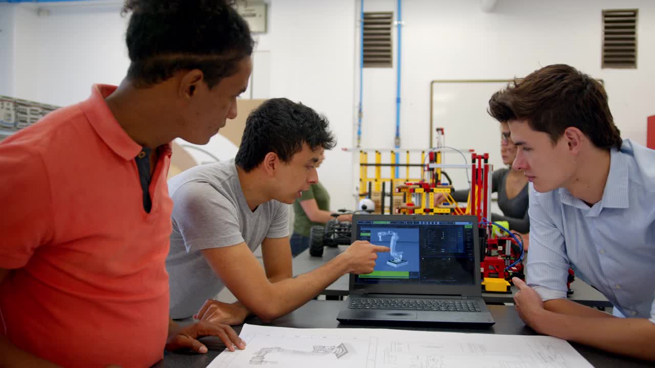 一组学生向男老师演示了一个项目，向他展示了笔记本电脑的屏幕和机械手臂的蓝图视频下载