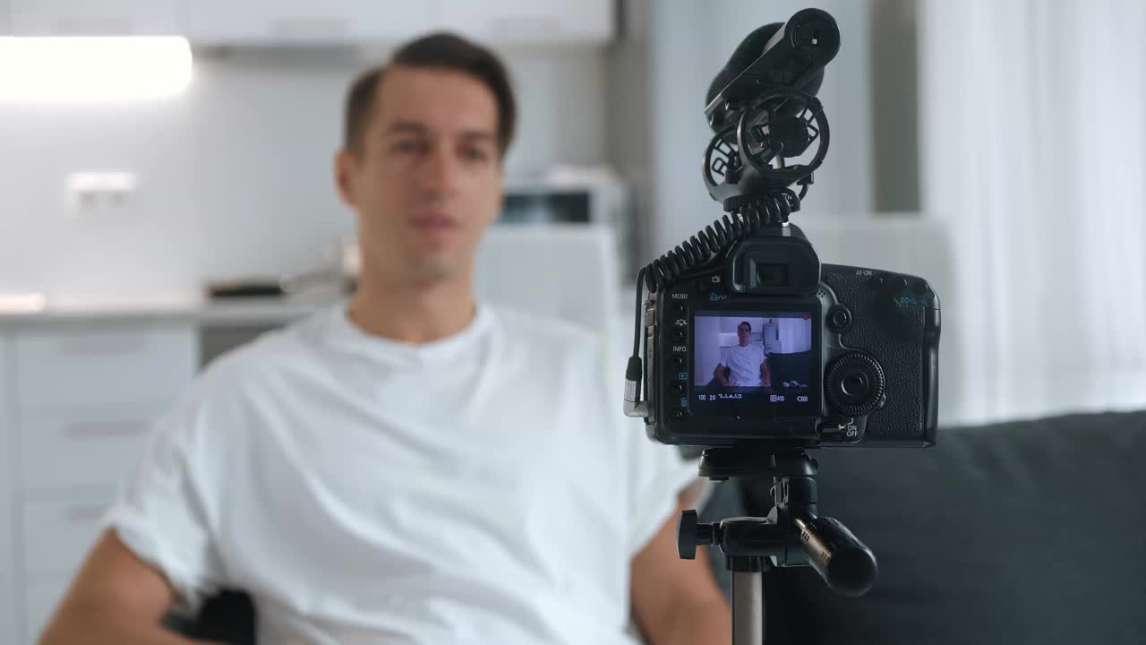 千禧一代的博主或视频博主用专业相机拍摄新的视频博主视频，安装在三脚架上坐在家里的沙发上。视频下载