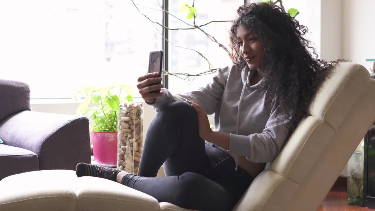 一名年轻女子在家里坐在沙发上与母亲视频通话视频下载