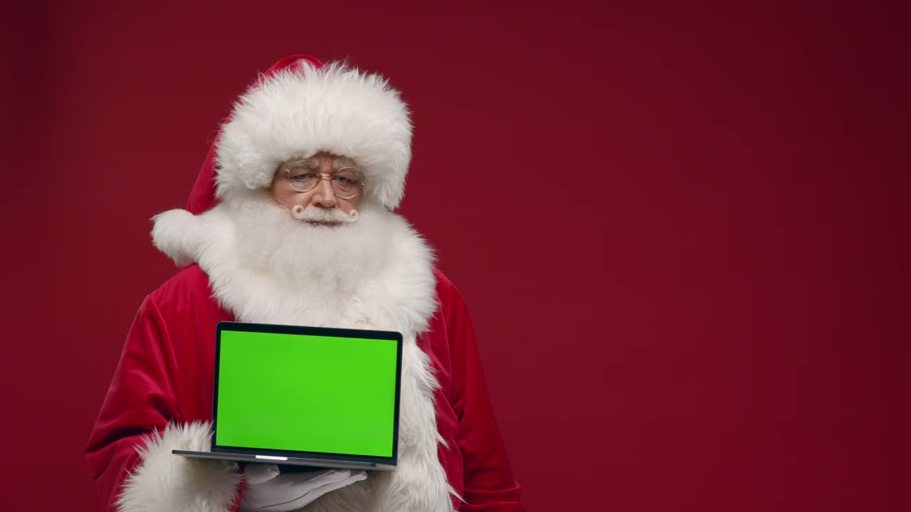 惊讶的圣诞老人手里拿着笔记本电脑，用不同的情绪，在红色的背景下，在摄像机中显示色度键视频下载