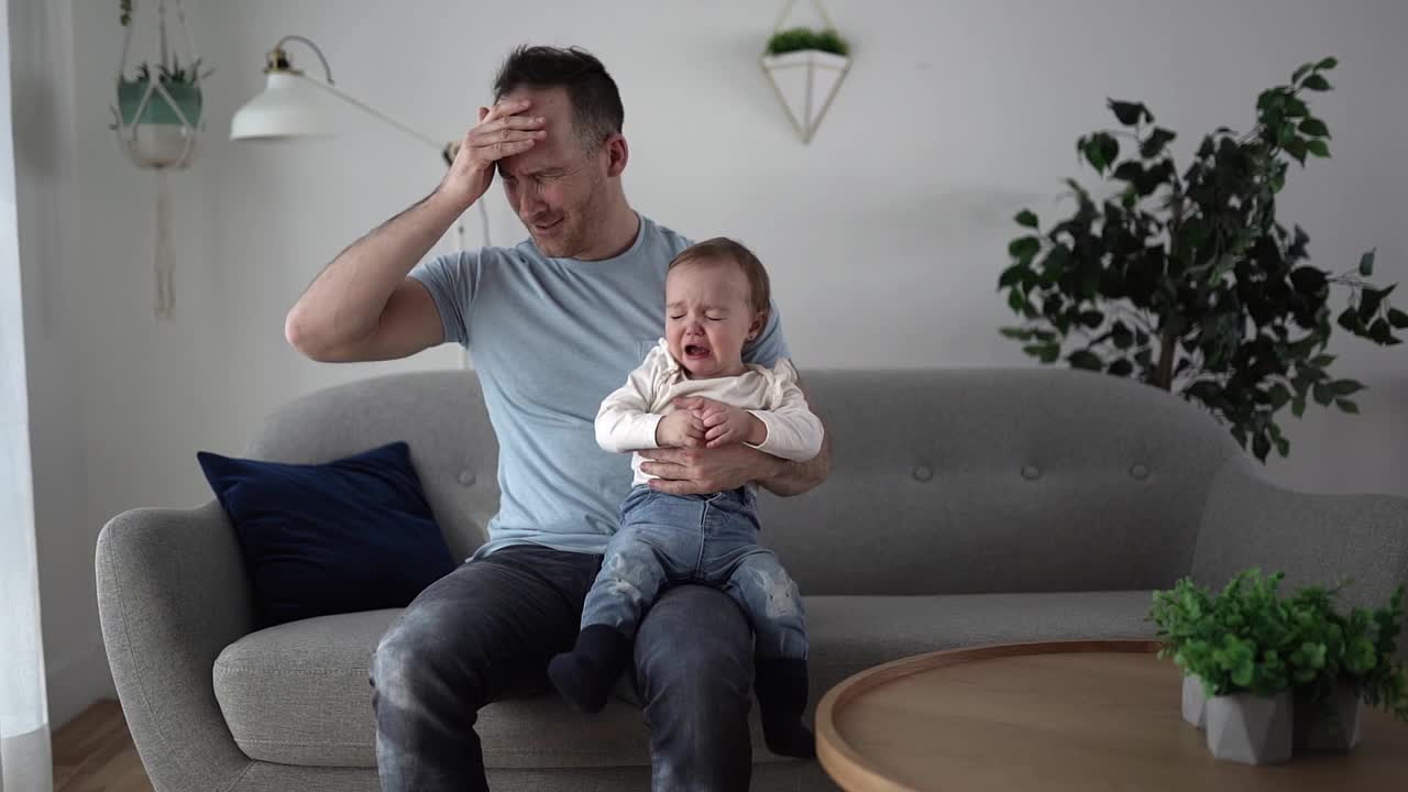 一个男人抱着一个尖叫的婴儿，他的父亲头痛视频素材