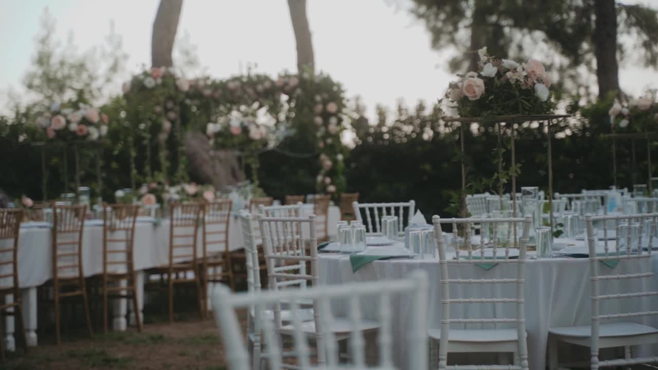 令人惊叹的婚礼布置在花园，白色桌布和木制椅子的桌子。美丽的节日气氛。花园里到处都是粉红色和白色的玫瑰。视频下载