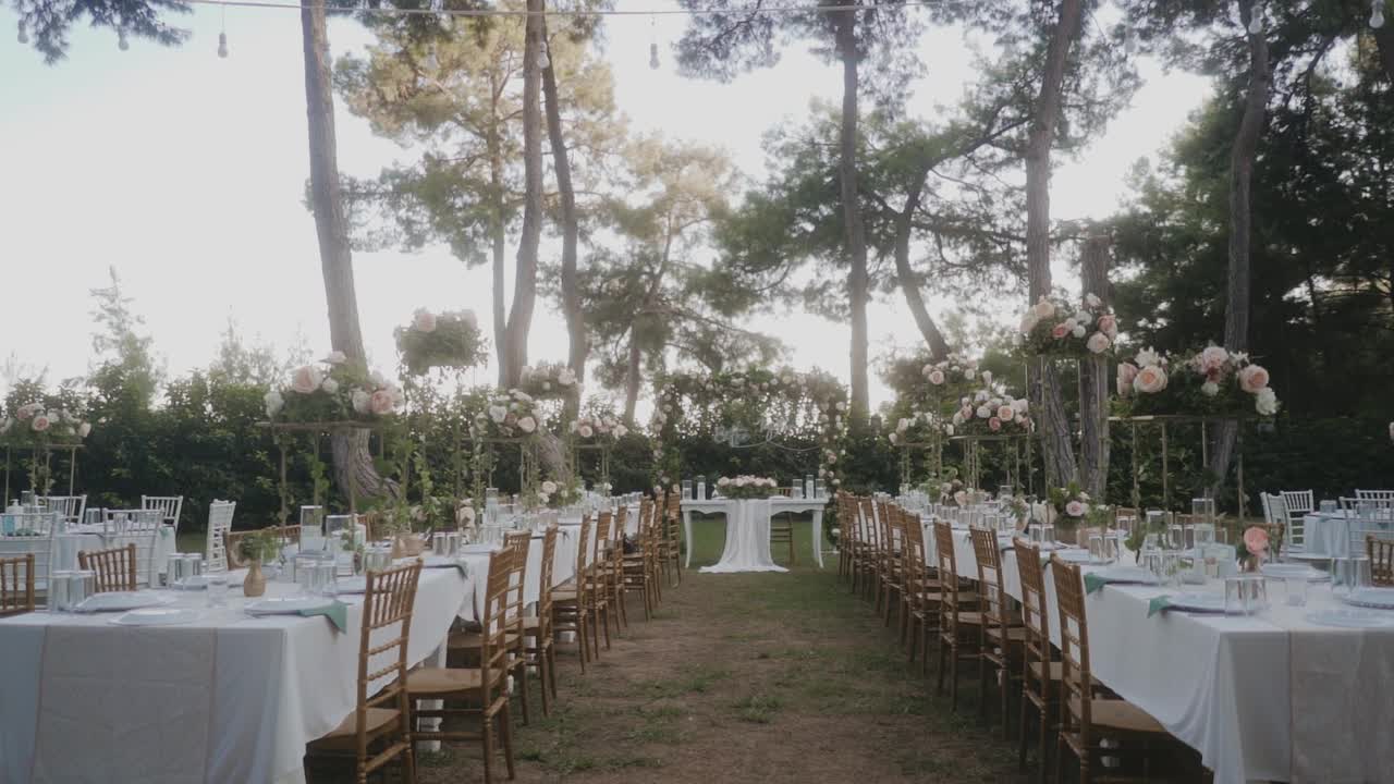 令人惊叹的婚礼布置在花园，白色桌布和木制椅子的桌子。美丽的节日气氛。花园里到处都是粉红色和白色的玫瑰。视频素材