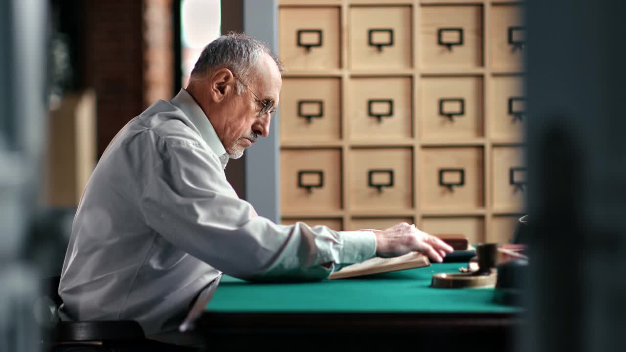 一位沉思的老人坐在复古的书桌旁读着课文纸书视频素材