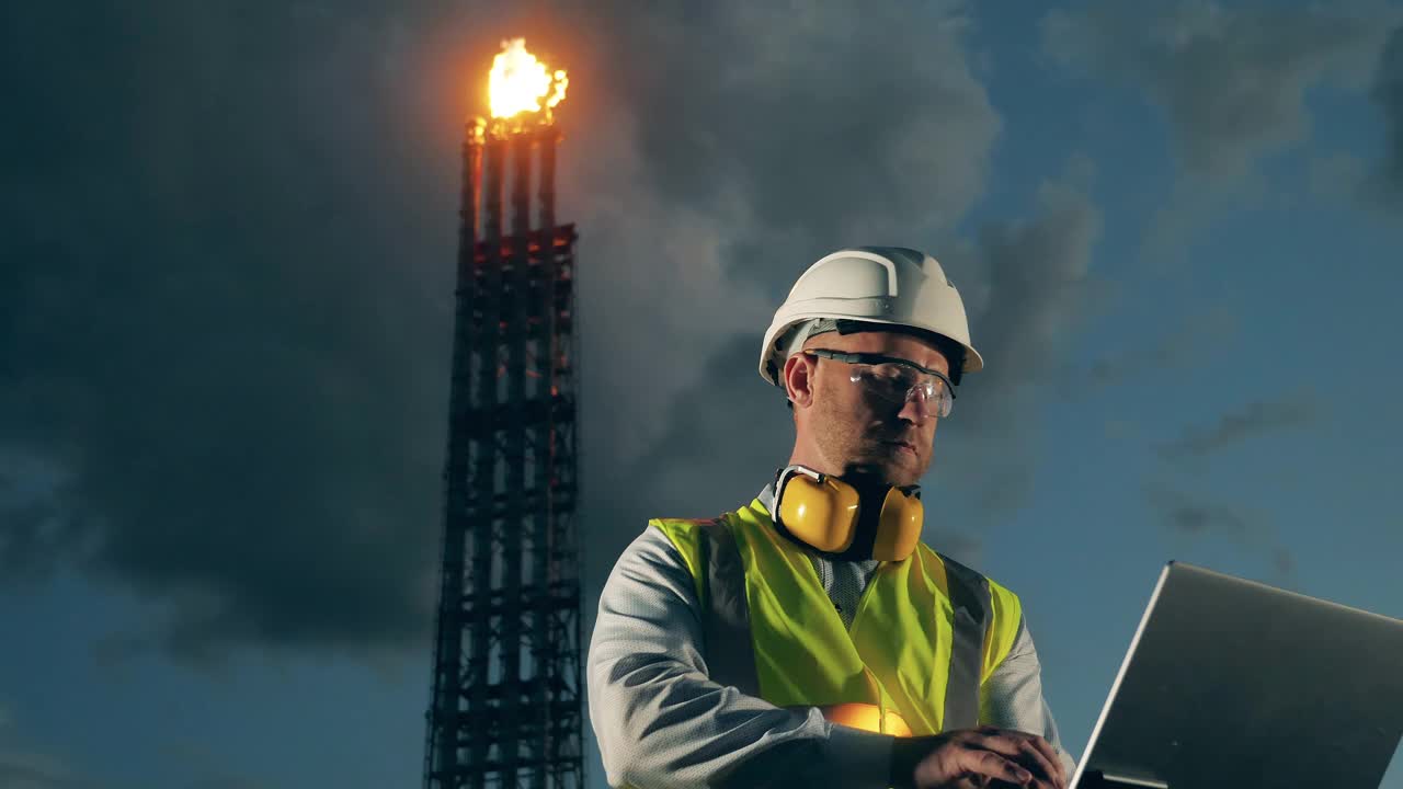 石油专家正在火炬堆附近操作一台笔记本电脑视频素材