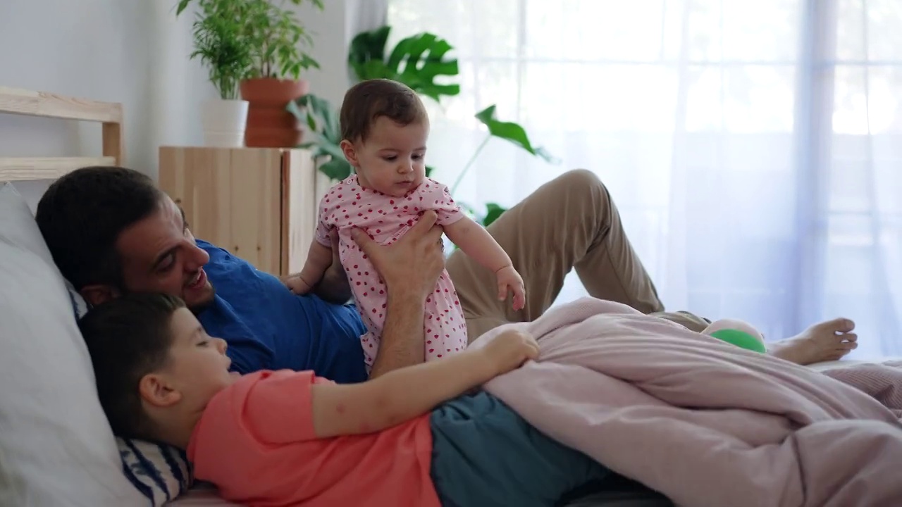 父亲在床上陪着女儿和蹒跚学步的儿子玩耍视频素材