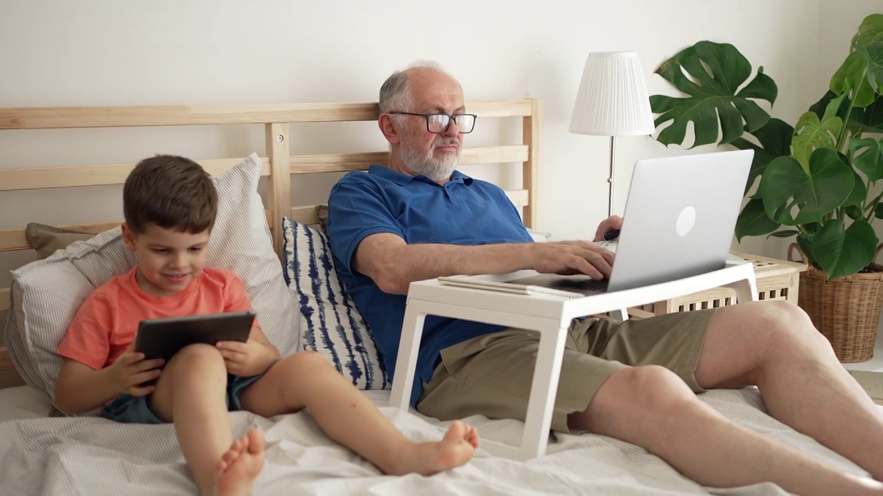 爷爷在笔记本电脑上工作，孙子在平板电脑上玩电子游戏视频素材