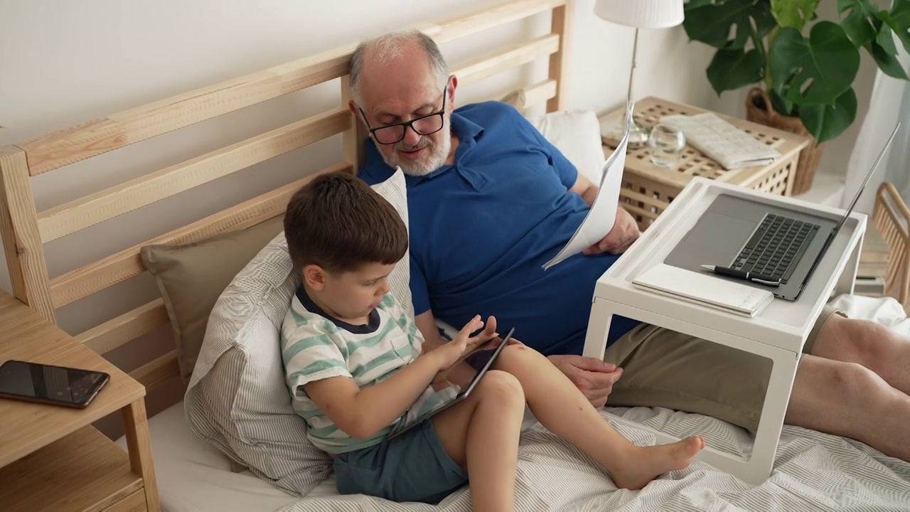 爷爷在笔记本电脑上工作，孙子在平板电脑上玩电子游戏视频素材