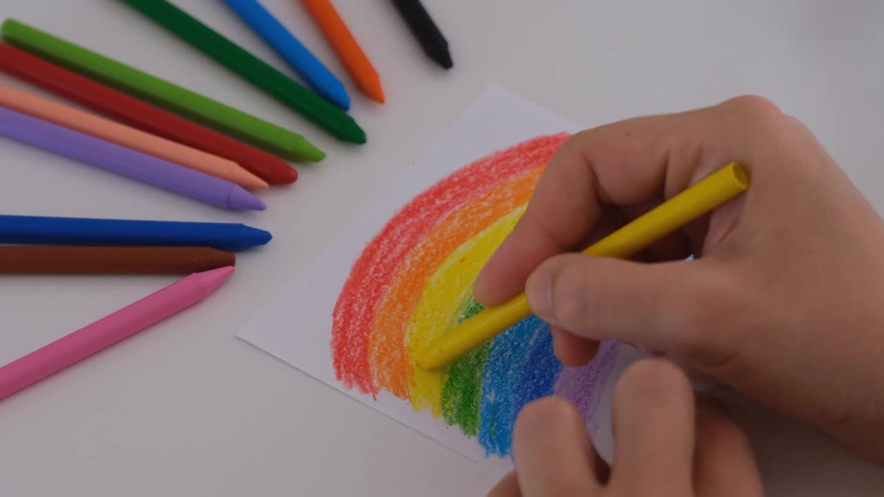 一个女人正在用黄色蜡笔给一幅彩虹画上色。视频下载