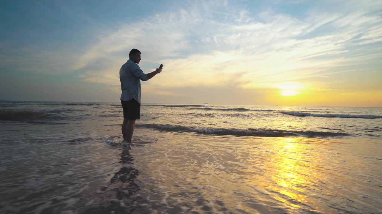 年轻的年轻人站在日落、日出的海边，用智能手机自拍，度假和夏季旅行视频素材