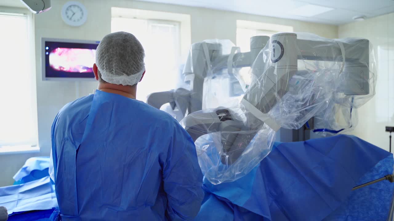 现代化手术室里的高科技设备。外科医生在医疗机器人附近的后视图。医生用机器人系统做手术，看着屏幕。视频下载