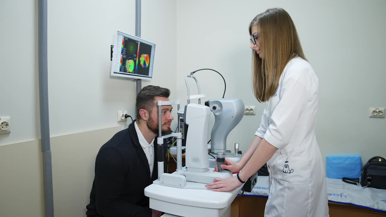 一个英俊的男人在诊所检查眼睛。年轻女医生用现代眼科仪器为病人检查视力。视频下载
