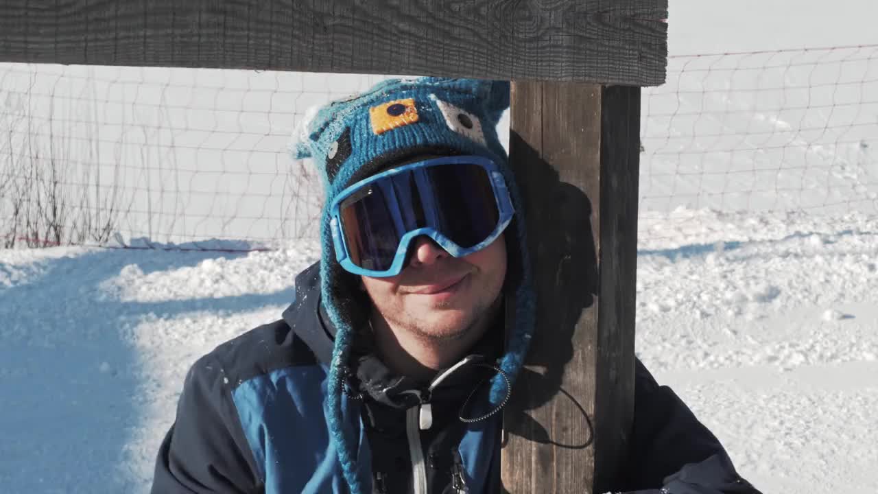 一个快乐而疲惫的滑雪者站在一根木杆前做鬼脸。视频下载