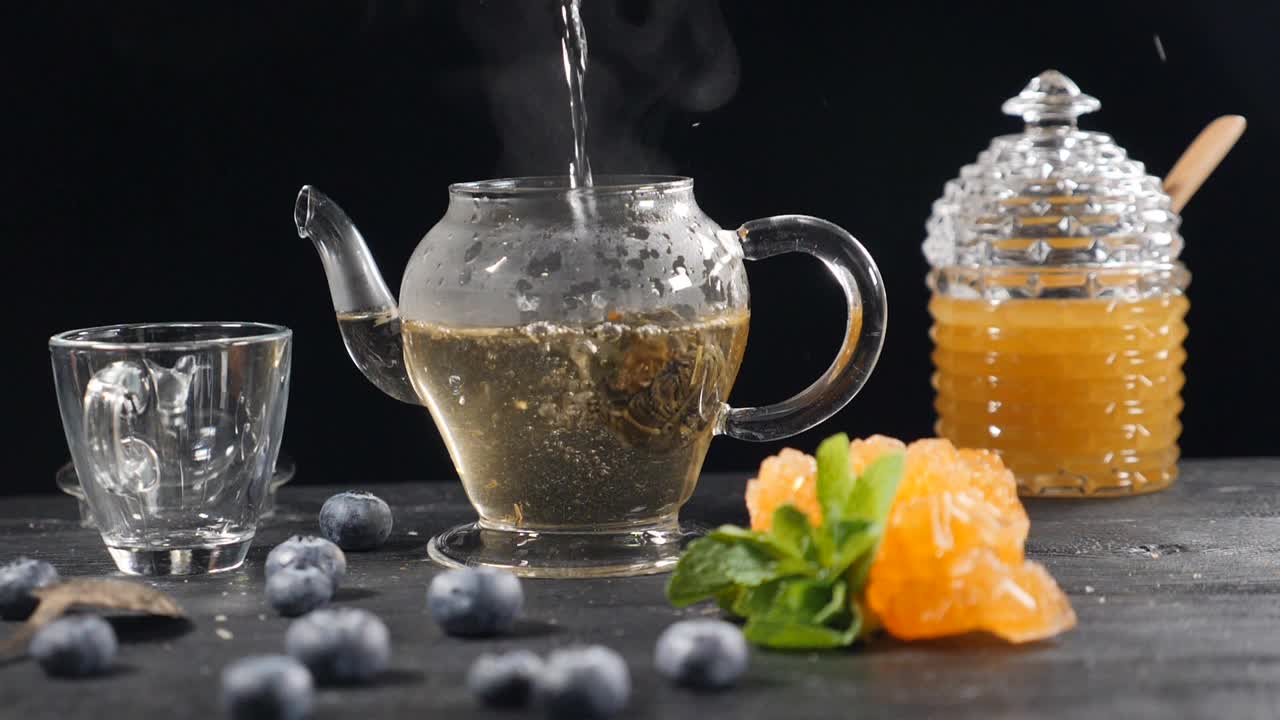 茶酿造仪式。绿色中国茶花玻璃茶壶在木制背景。蓝莓，玻璃罐和蜂蜜。倒开水。缓慢的运动。在高清拍摄视频素材