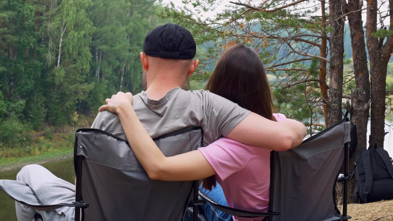 一对相爱的情侣坐在森林里的扶手椅上，拥抱着，享受着大自然，看着从悬崖到河里的风景。丈夫和妻子在森林里远足。家庭中的爱情关系视频下载