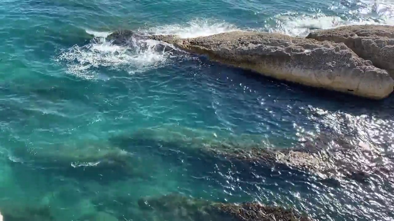 夏天，蓝绿色的海浪拍打着布满岩石的地中海海岸。闪闪发光的海水表面。地中海多岩石的海岸线。透明的翠绿色水。视频素材