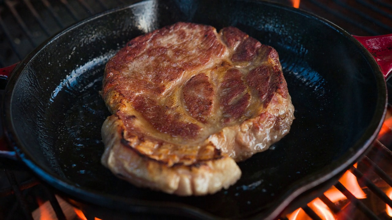 美味的牛排在铸铁煎锅上的明火烧烤视频下载