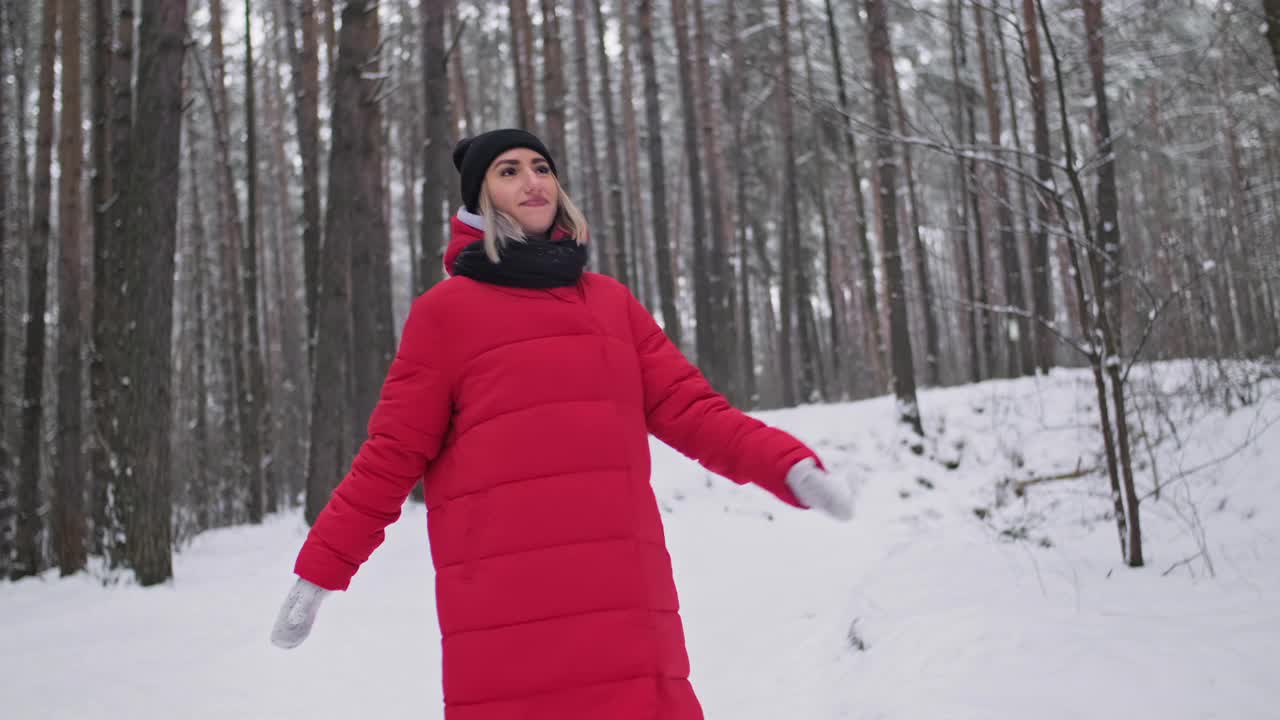 快乐的年轻女子在森林里享受冬天。穿着红色外套的女性在旋转。视频下载
