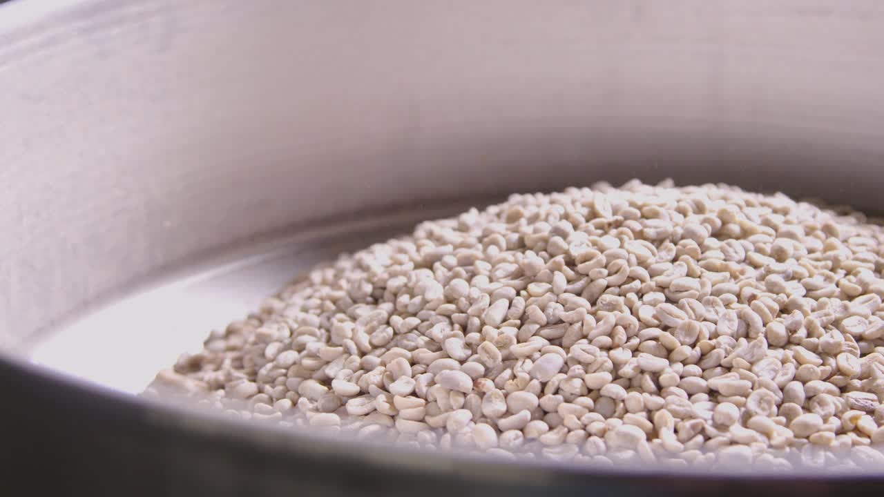 手持式拍摄的一堆生咖啡豆在一个专业的工业咖啡烘焙机准备烤在一个咖啡烘焙工厂仓库视频下载
