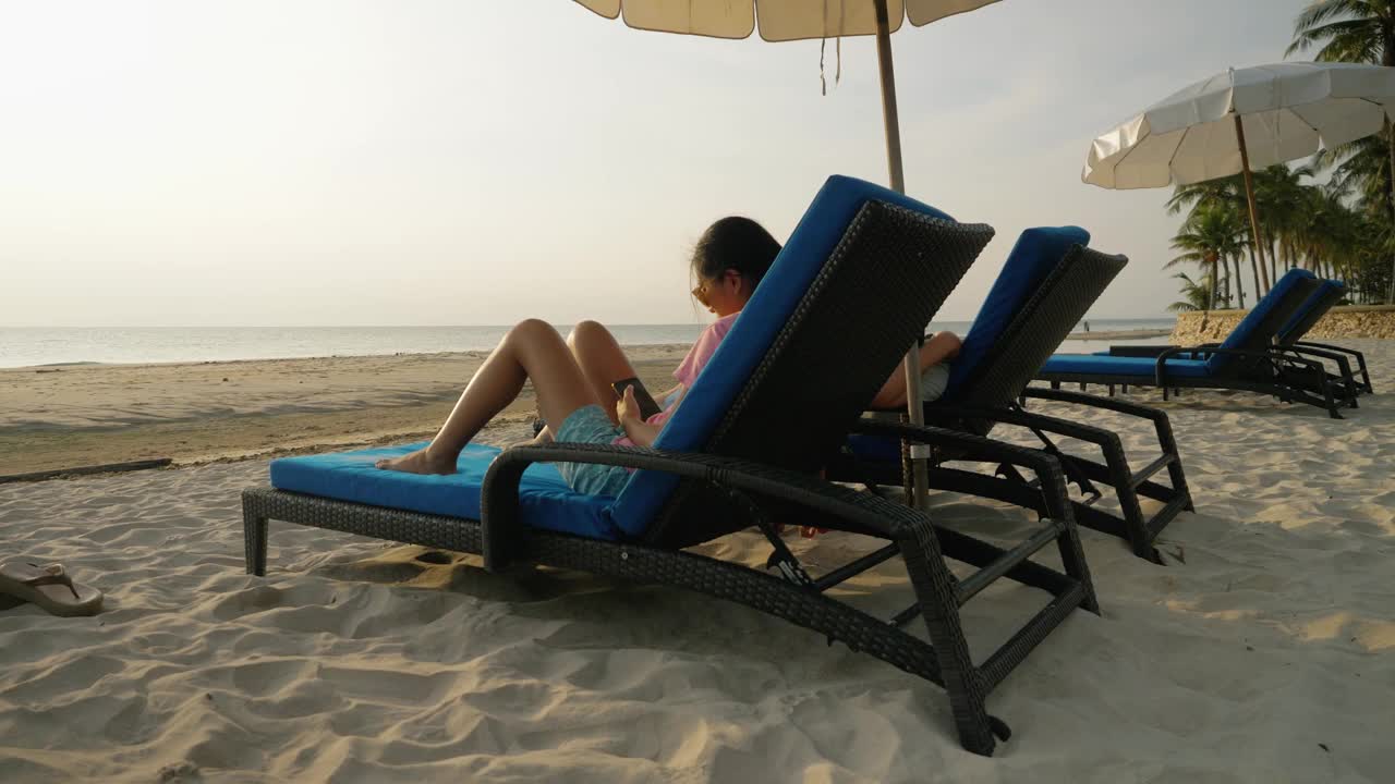 快乐的亚洲孩子戴着太阳镜在海滩椅上放松在早上在酒店或度假村度假，与家人，生活理念。视频下载
