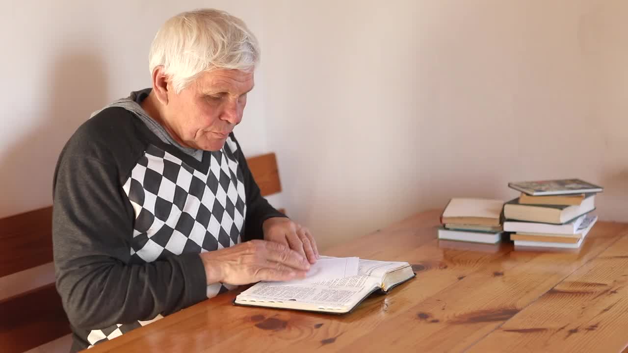 一个年长的男人正在祈祷，手里拿着一本旧圣经。视频下载