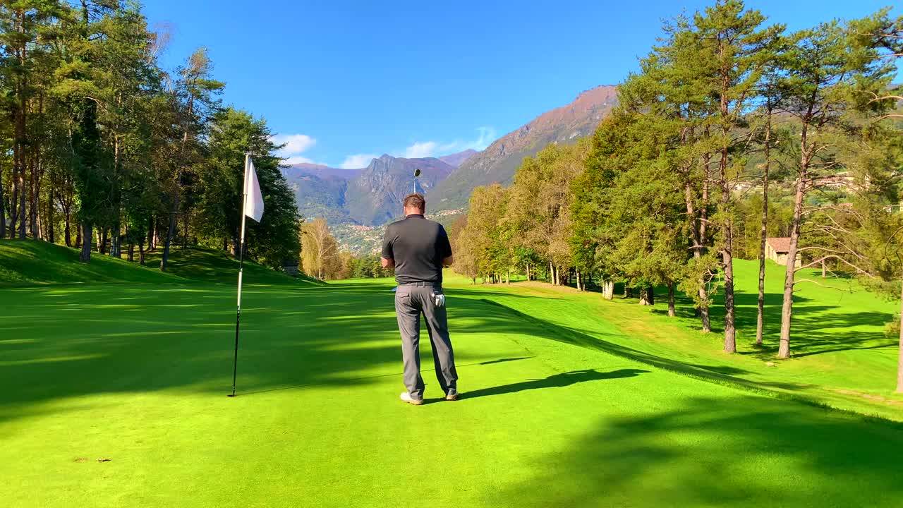 在意大利伦巴第的一个阳光明媚的日子里，高尔夫球手在与山景相映的果岭上推杆。视频素材