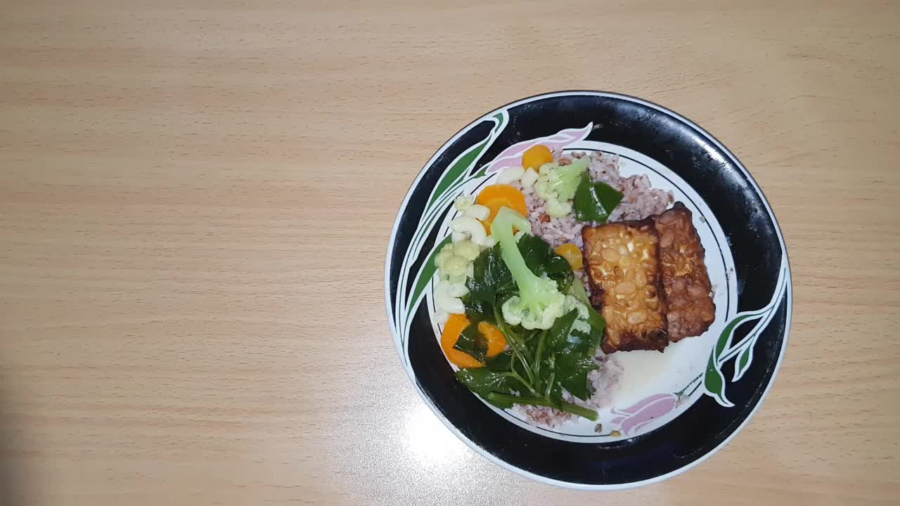 这是一种印尼蔬菜汤，由胡萝卜、花椰菜、芹菜、韭菜、红米饭和炒豆豉组成。盛在木制纹理背景的碗里。复制空间，选择性聚焦视频下载