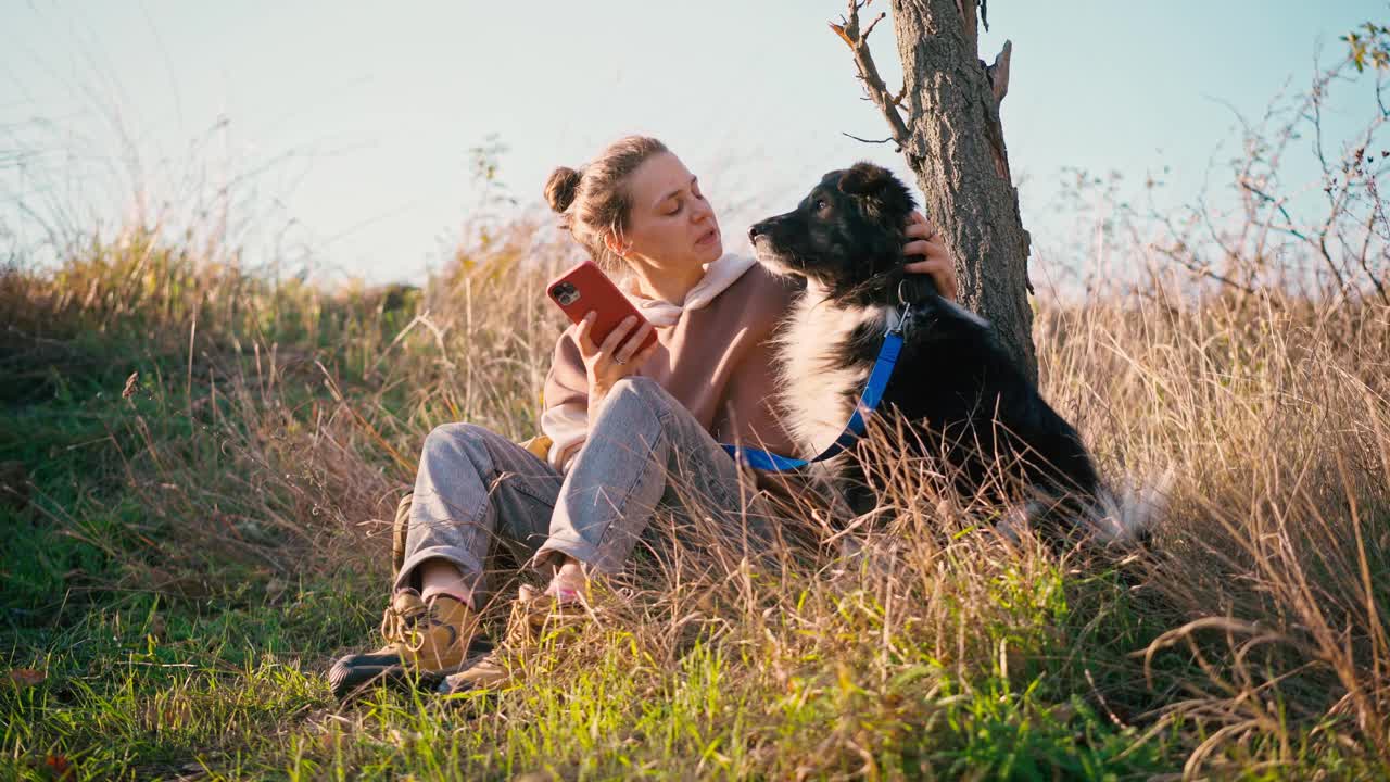 一位年轻的成年女子和她的狗狗坐在山上自拍视频素材