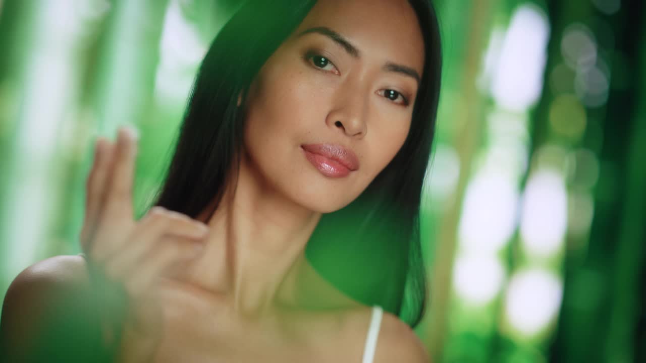 美丽的亚洲女人肖像轻轻应用面霜。年轻的成年女性使用科学先进的天然化妆品护肤品使她的皮肤柔软，光滑。绿色森林背景视频下载