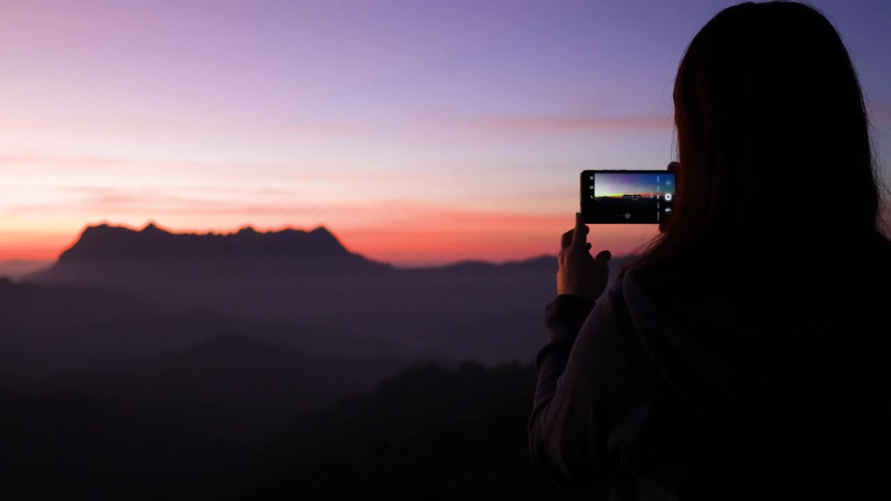 女旅行者在日出的时候在山上拍摄一个美妙的地方视频素材