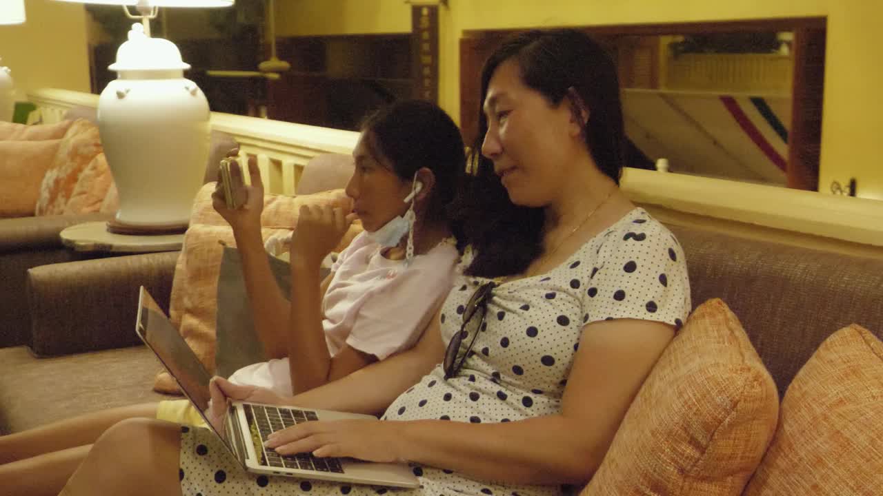 亚洲母亲在酒店大堂使用笔记本电脑，在度假期间与女儿在夜间工作，在任何地方工作的生活理念。视频素材