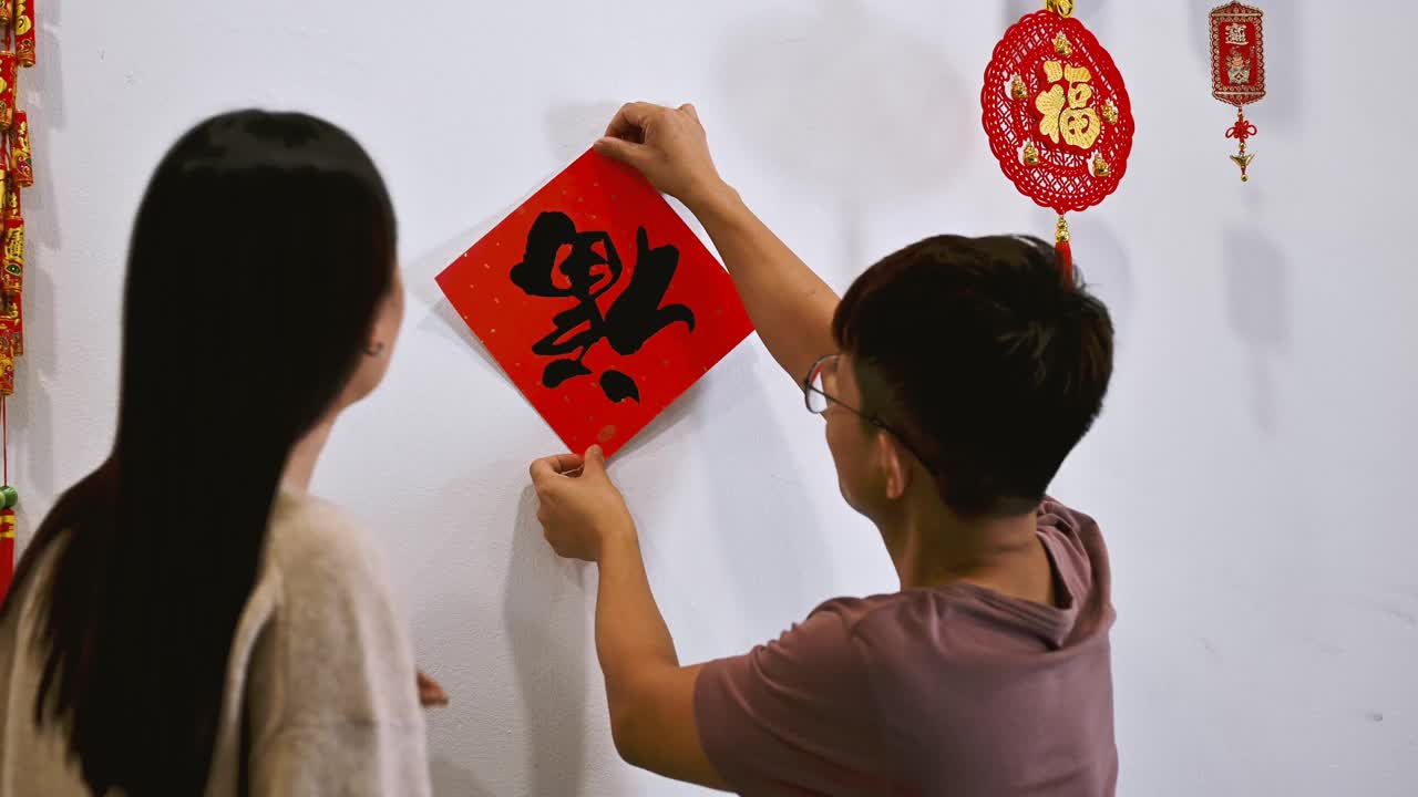 亚洲的中国夫妇装饰他们的房子，并张贴中国对联，为即将到来的中国年祝福视频素材