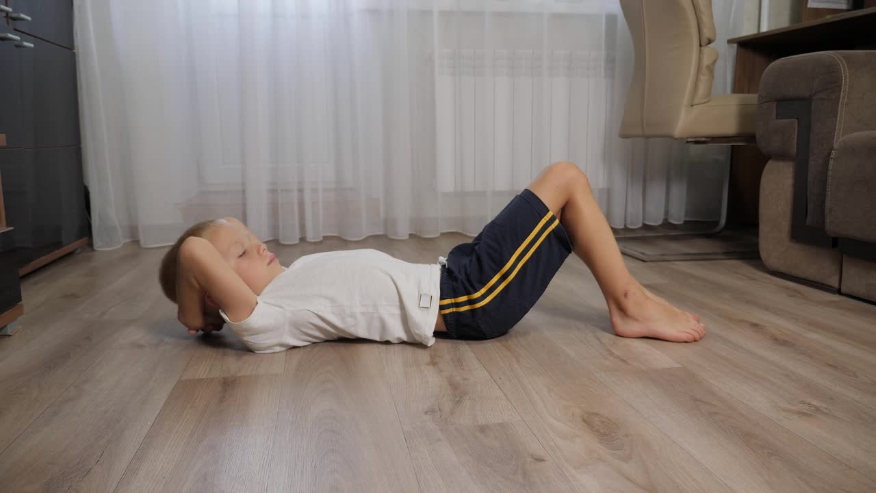 一个八岁的小男孩在家里的地板上摇着他的腹肌。视频下载