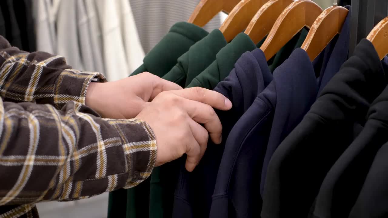 一个男人在衣架上选择了一件彩色运动衫。视频素材