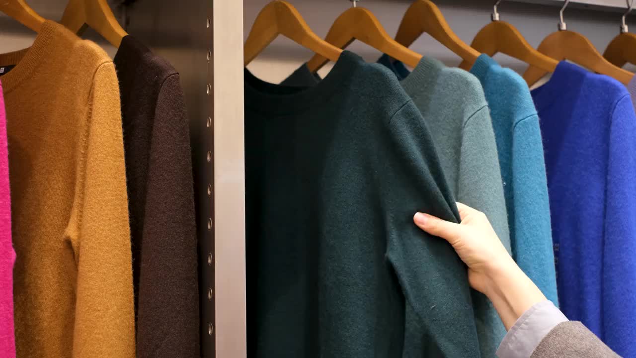 女手在商店里挑选木制衣架上的彩色毛衣。视频素材