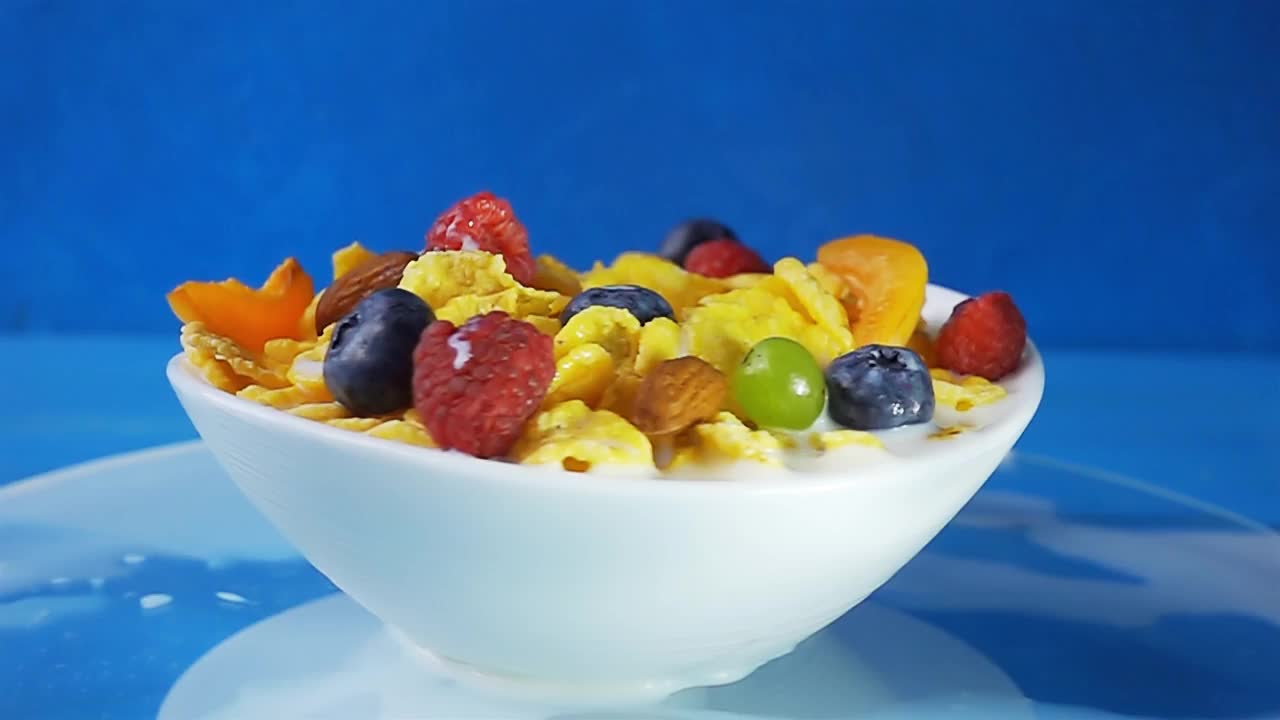 牛奶倒进黄色的玉米片里，配上各种新鲜浆果，包括蓝莓、覆盆子、葡萄和杏仁。4k原始慢动作速度斜坡视频。视频素材