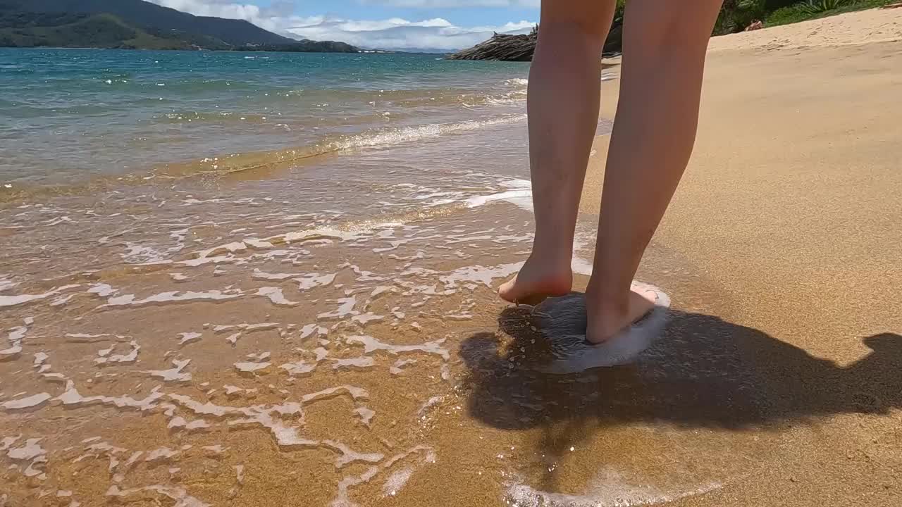 女性的腿在透明的海水附近行走。视频下载