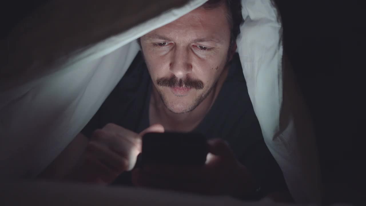 一个男人在深夜使用她的智能手机。视频下载