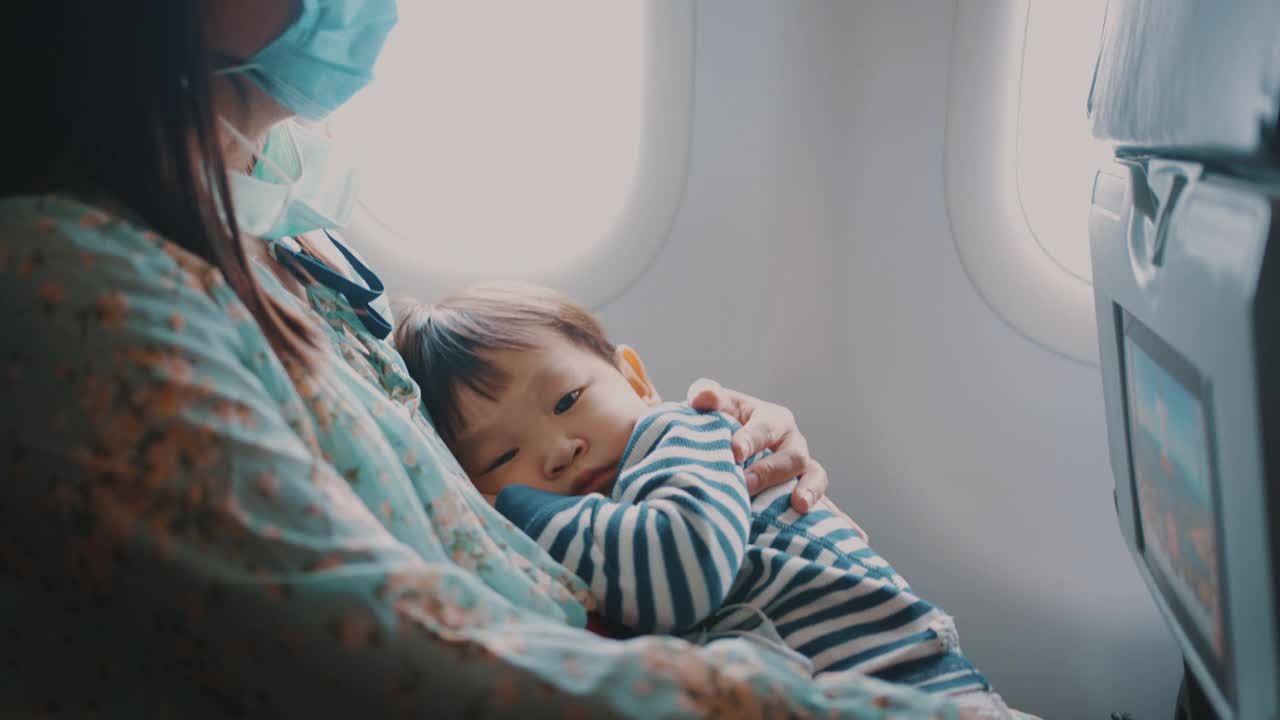 乘飞机旅行时，男孩睡在母亲的怀里。视频下载