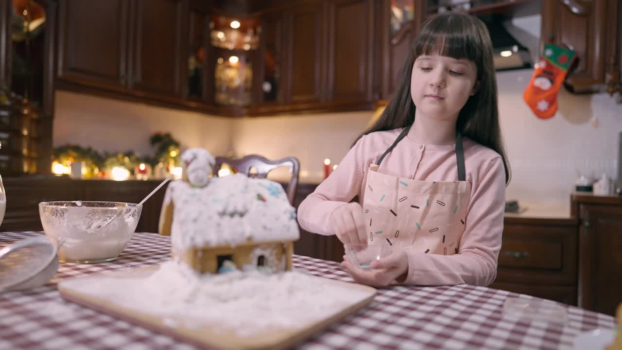 在家里的厨房里，漂亮专注的女孩用糖粉装饰姜饼屋。自信的高加索孩子在围裙烹饪美味的传统圣诞甜点在新年视频素材