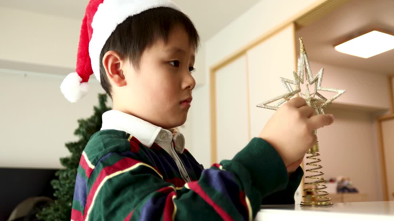 一个男孩组装了一个星星装饰物放在圣诞树的顶部视频下载