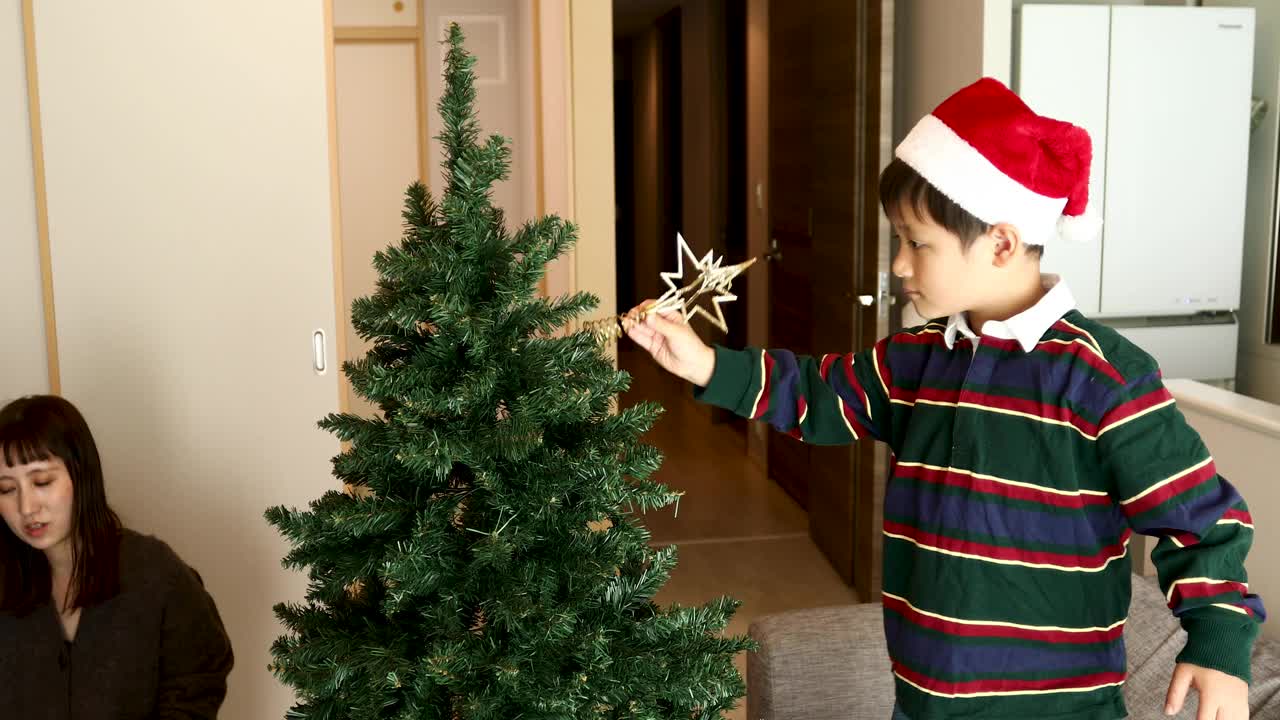 一个男孩举起一颗星星，准备放在圣诞树的顶端视频下载