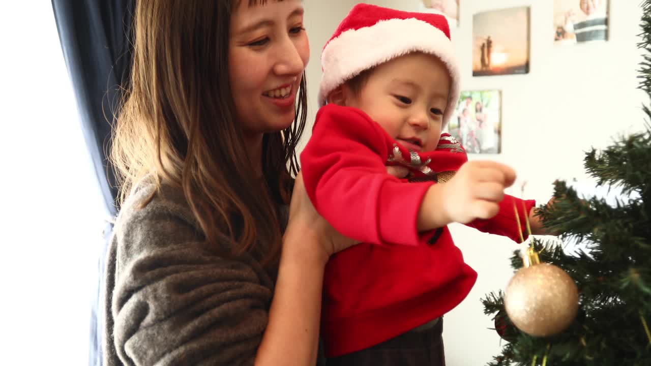 一个小男孩被他的妈妈抱起来，他正试图装饰圣诞树视频下载