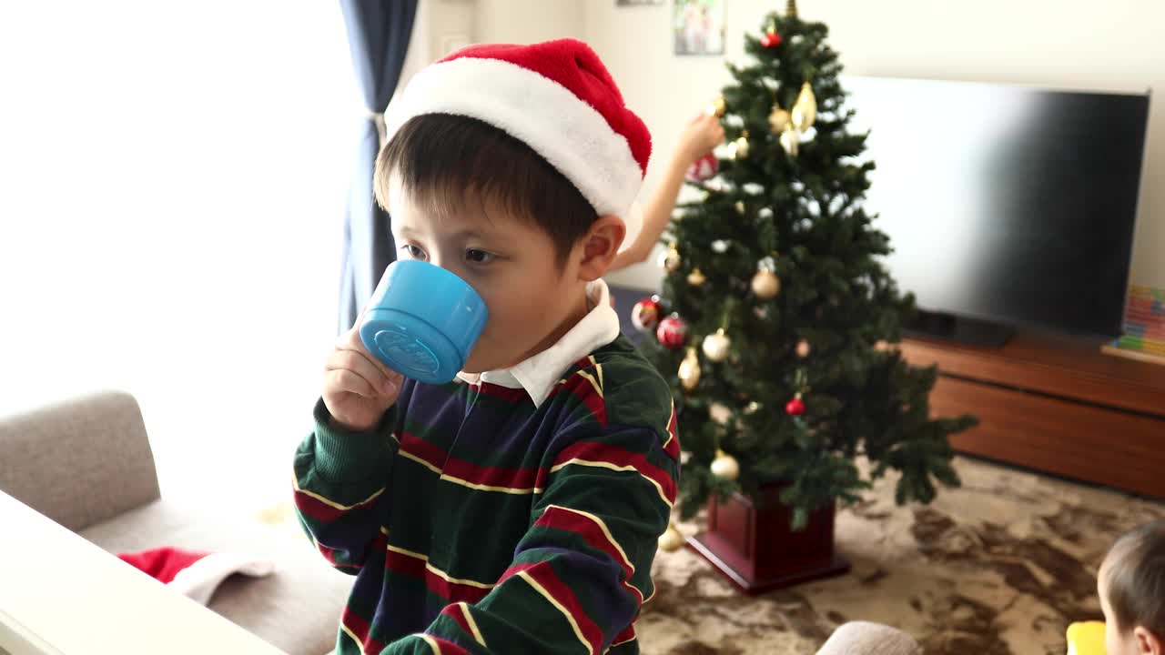 一个男孩在装饰着圣诞树的客厅里喝水视频下载