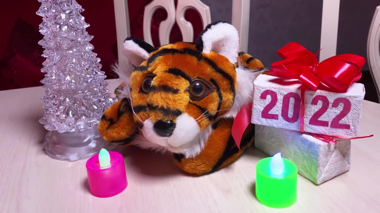 象征2022年的老虎，房间里圣诞树旁的白色桌子上摆放着蜡烛和印有2022字样的礼盒。视频下载